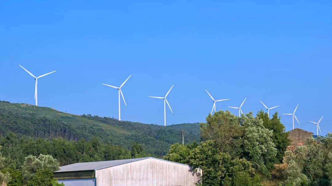Mehrere kleine Windturbinen sind auf einem grünen Hügel unter blauem Himmel positioniert, mit Bäumen und einem weißen Gebäude im Vordergrund - ein Beispiel moderner Energiegewinnung in vielfältigen Anwendungsmöglichkeiten.