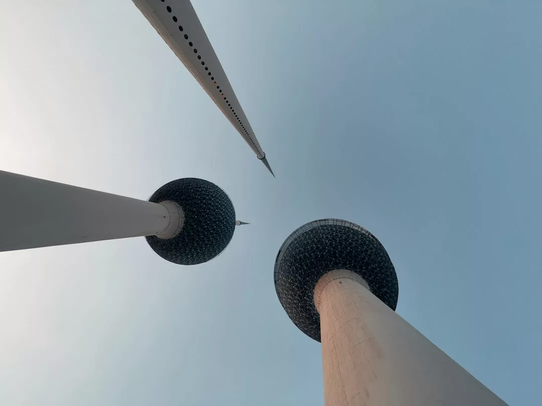 Blick von oben auf die drei Kuwait-Türme bei klarem Himmel. Ihre kugelförmigen Aussichtsplattformen und spitz zulaufenden Strukturen werfen einen markanten Schattenwurf, der an moderne Windkraftanlagen erinnert.