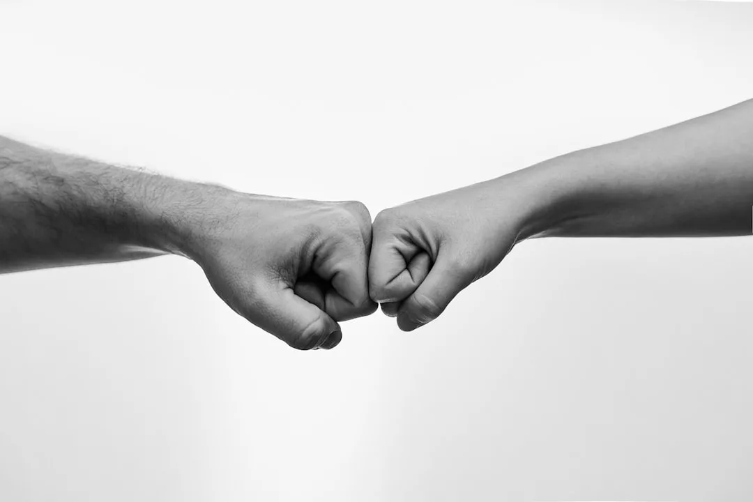 Zwei Menschen geben sich einen Fist Bump - ein Symbol für Beziehungskompetenz und eine gesunde Partnerschaft, festgehalten in Schwarz-Weiß vor weißem Hintergrund.