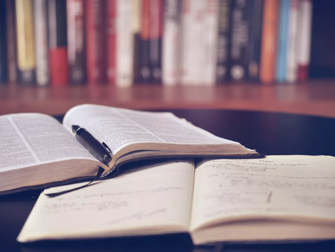 Ein aufgeschlagenes Buch und ein Notizbuch mit handschriftlichen Notizen liegen auf einem Tisch, ein Stift ruht auf dem Buch - perfekt für die Erkundung von Ratgebern oder neuen Büchern passend zur Lebenslage, mit einem verschwommenen Bücherregal im Hintergrund.