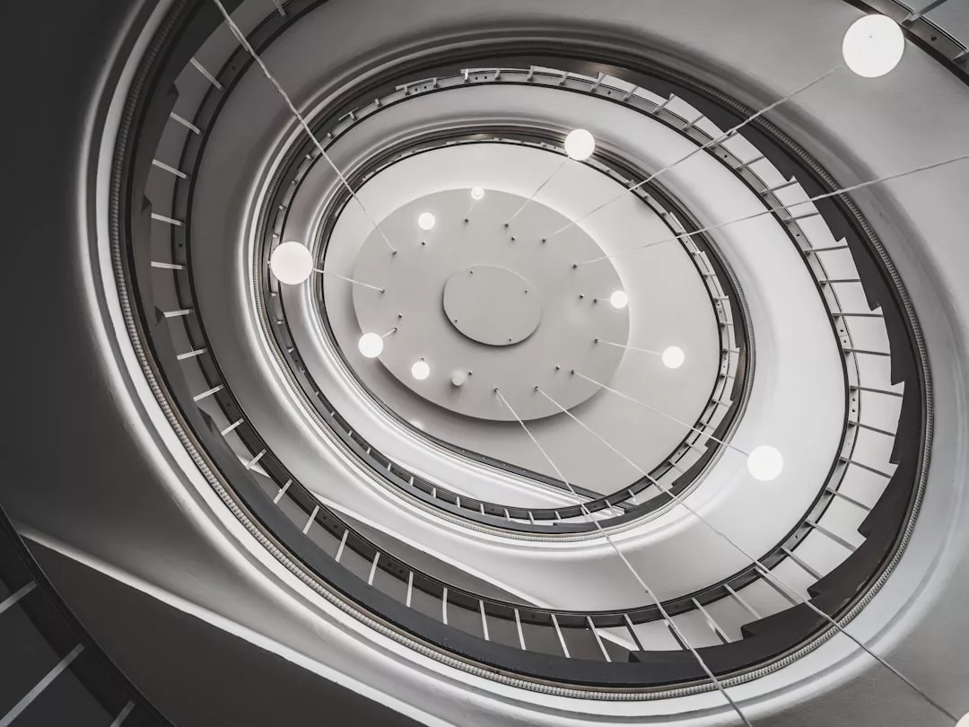 Blick auf eine moderne Wendeltreppe mit kreisförmigen, von der Decke hängenden Lichtern, die ein geometrisches Muster bilden - ein Symbol für Aufstieg und Erfolg in der Unternehmenswelt.