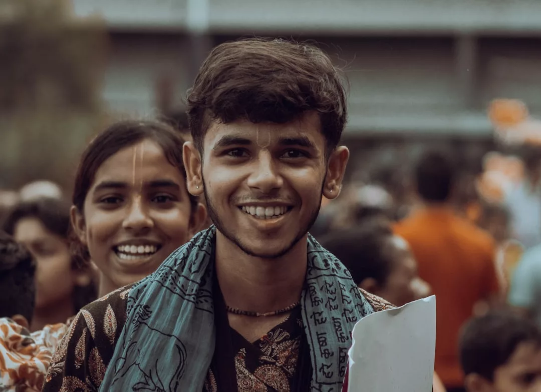Ein junger Mann lächelt in die Kamera und hält Papiere über den Hinduismus in der Hand. Hinter ihm steht eine junge Frau in einer belebten Umgebung im Freien, was auf eine Einführung oder eine umfassende Einführung in das Thema hindeutet.
