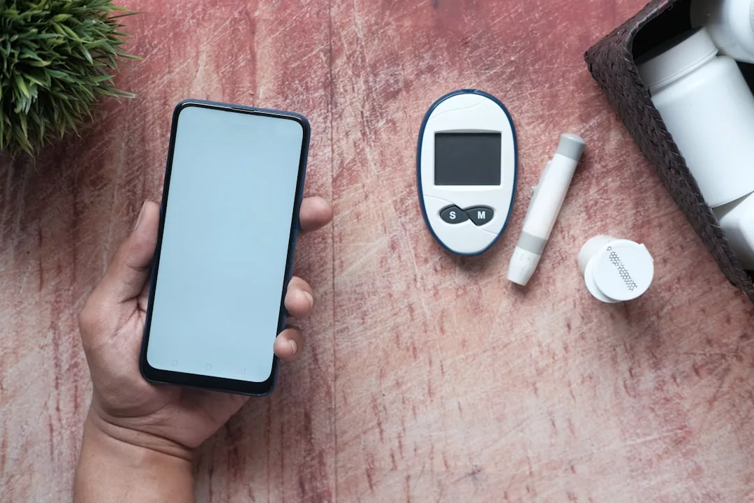 Eine Person hält ein Smartphone neben einem Blutzuckermessgerät, einer Stechhilfe und einem Teststreifenbehälter auf einer Holzfläche - Symbole für das tägliche Diabetes-Management und die Bedeutung einer gesunden Ernährung.