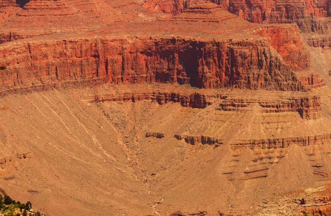 Erodierte Schichten roter und brauner Felsformationen in einem Wüstencanyon mit steilen Klippen und Sedimentmustern - dieses Naturwunder zieht Besucher aus aller Welt wegen seiner atemberaubenden Landschaft an.