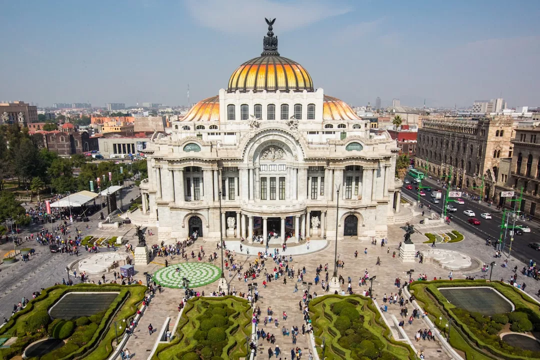 Luftaufnahme des Palacio de Bellas Artes in Mexiko-Stadt, einem Zentrum der Bildenden Kunst, mit seinem Kuppeldach, der verzierten Fassade und den Menschenmengen aus allen Schichten der Gesellschaft, die sich auf dem belebten Platz und in den Gärten davor versammelt haben.