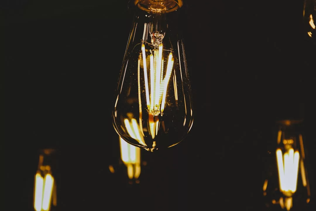 Nahaufnahme einer leuchtenden Edison-Glühbirne mit sichtbarem Glühfaden, die die Bedeutung von Energieforschung für die Zukunft symbolisiert, während andere ähnliche Glühbirnen im dunklen Hintergrund verschwommen sind.