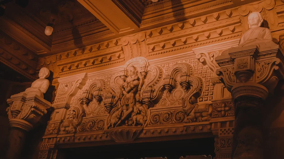 Aufwändig geschnitzte Steinwand mit detailliertem Relief einer Gottheit im Zentrum, flankiert von zwei Statuen auf verzierten Säulen, unter einer dekorativen Decke - ein bemerkenswertes Zeugnis der Kunstgeschichte inmitten der Einflüsse der modernen Gesellschaft.