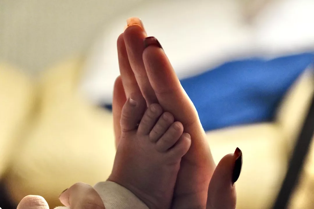 Eine Nahaufnahme einer Erwachsenenhand und eines Babyfußes, die zusammengedrückt werden, symbolisiert die Bedeutung von Berührung in der Säuglingspflege, da die Zehen des Babys mit den Fingern des Erwachsenen übereinstimmen.