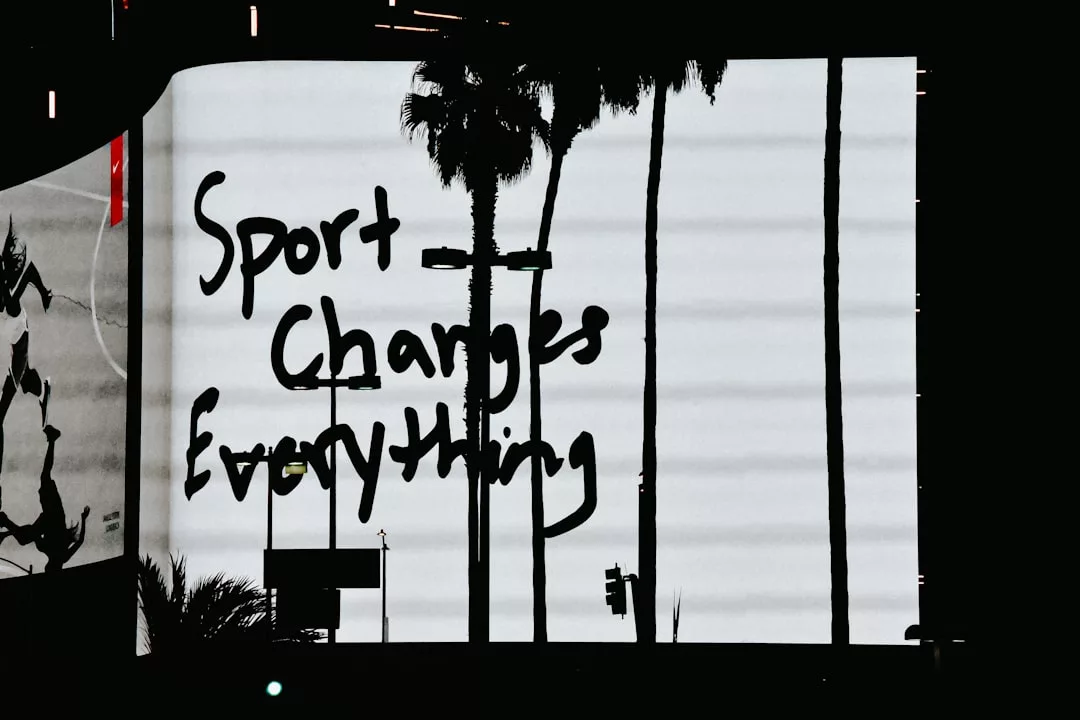 Auf einer Plakatwand steht in schwarzen Buchstaben der handgeschriebene Satz "Sport verändert alles", der die Bedeutung von Sportpsychologie hervorhebt, mit Palmensilhouetten im Vordergrund.
