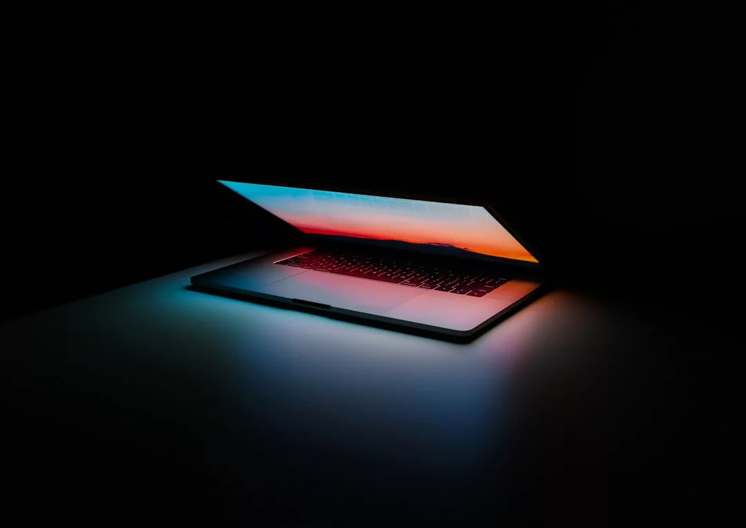 Auf einer dunklen Fläche steht ein teilweise aufgeklappter Laptop, dessen Bildschirm einen Farbverlauf zeigt und ein sanftes Licht auf die Tastatur wirft - ein Sinnbild für moderne Bildung in der heutigen technologiegetriebenen Welt.