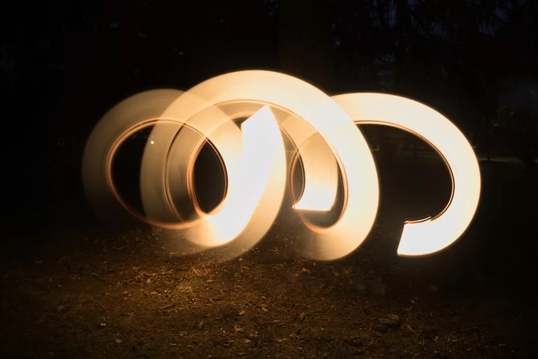 Gekrümmte Spuren warmen Lichts bewegen sich in Schleifen vor einem dunklen Hintergrund und bilden abstrakte Muster über einem schwach beleuchteten Grund - wie die wirbelnde Energie, die oft mit Zwillingsflammen in Verbindung gebracht wird.
