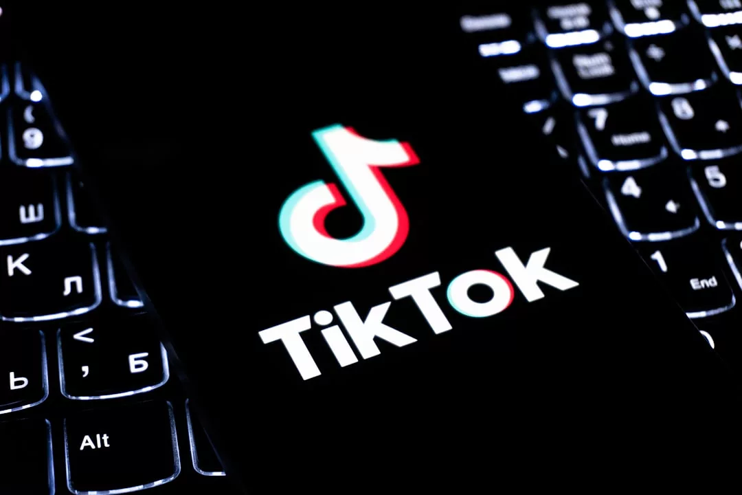 Ein Smartphone, auf dessen Bildschirm das TikTok-Logo und der Name der App angezeigt werden, steht auf einer beleuchteten Computertastatur und symbolisiert die Bedeutung digitaler Plattformen für eine erfolgreiche Bewerbung oder Online-Bewerbung.