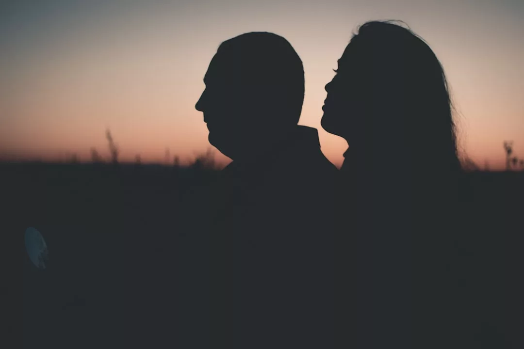 Die Silhouetten zweier Menschen, die bei Sonnenuntergang im Freien eng beieinander stehen, mit einem verblassenden Himmel im Hintergrund, erinnern an Themen der Beziehungstherapie im Kontext unserer modernen Gesellschaft.