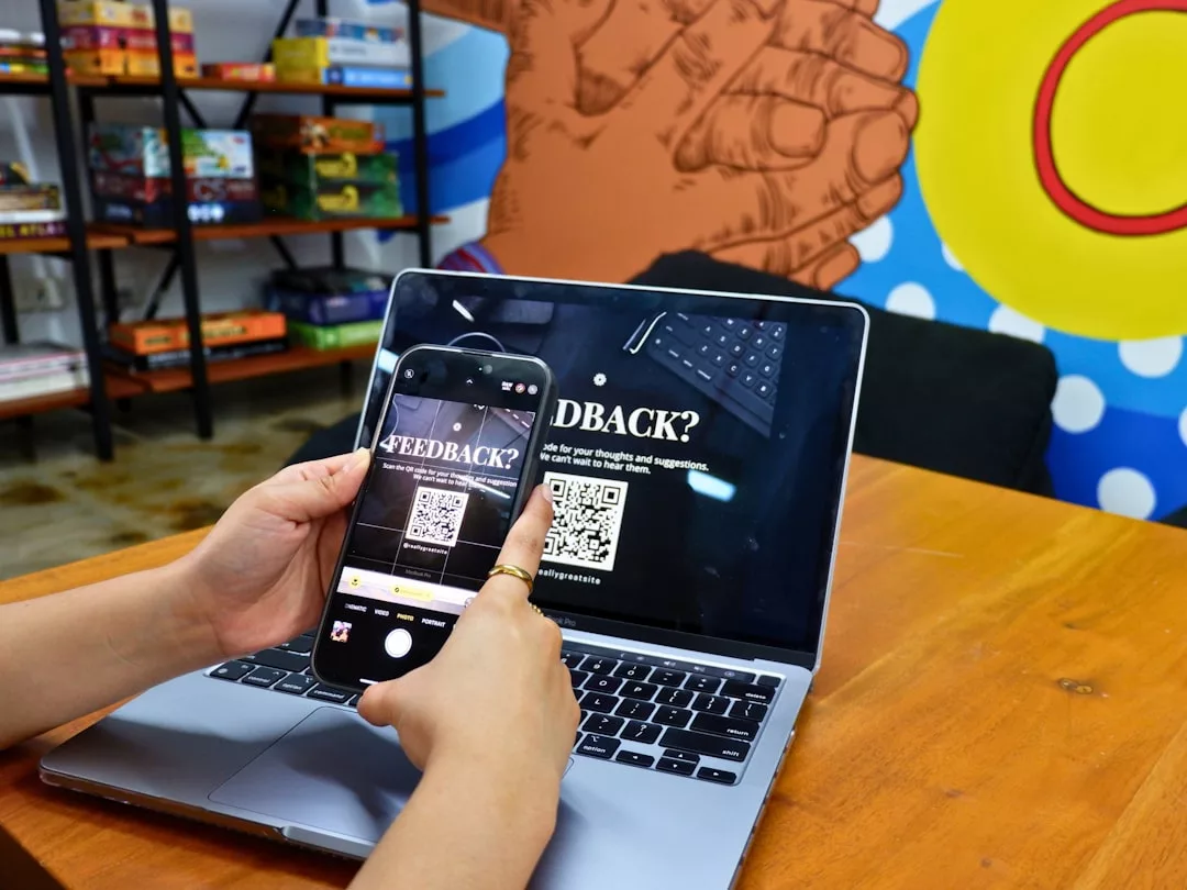Eine Person scannt einen QR-Code für Feedback beim Lernen, der auf einem Laptop-Bildschirm mit einem Smartphone angezeigt wird. Im Hintergrund sind Brettspiele und ein buntes Wandgemälde zu sehen.