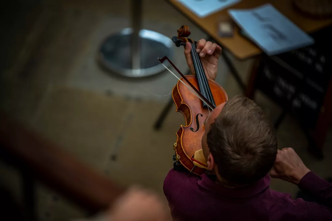 Eine Person, von oben gesehen, spielt eine Geige mit einem Bogen; im Hintergrund sind ein Notenständer und Notenblätter zu sehen, die die Bedeutung von Musik in der frühkindlichen Entwicklung unterstreichen.