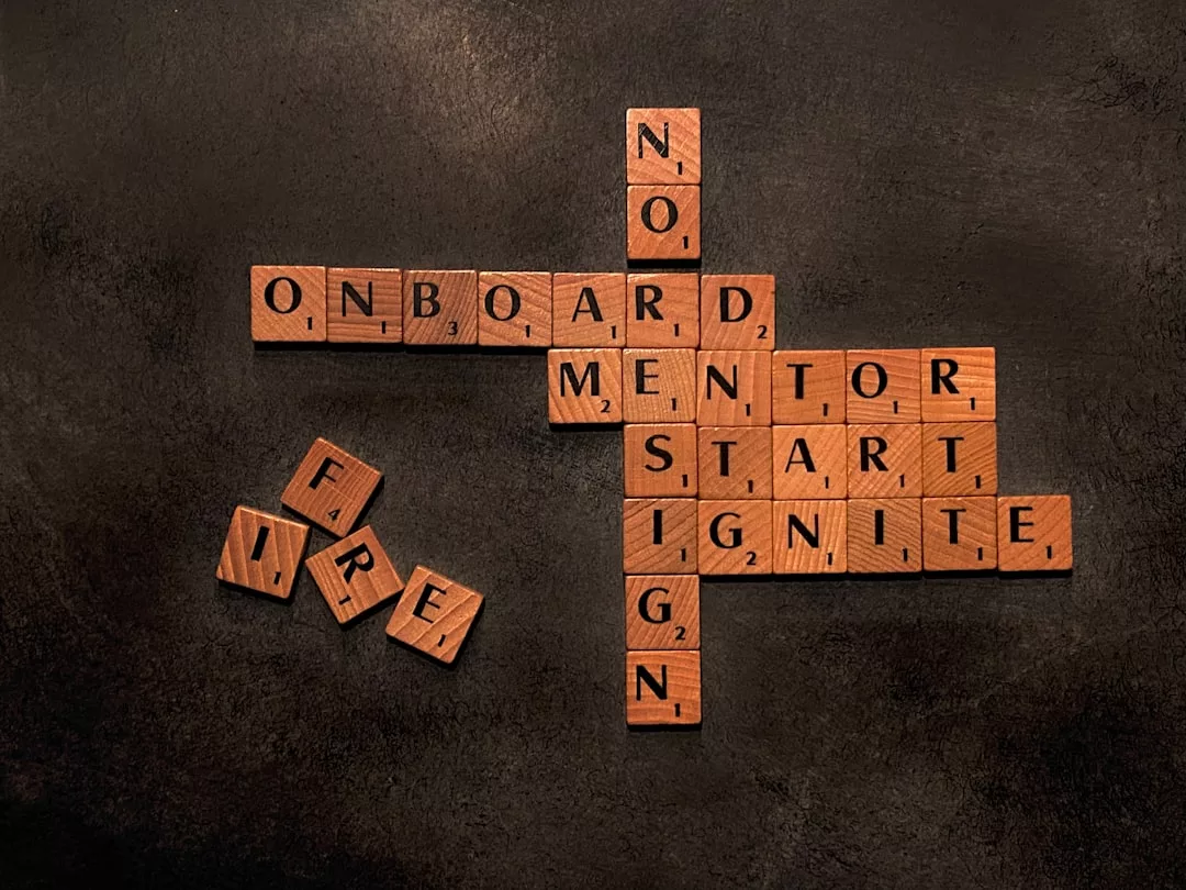 Hölzerne Scrabble-Kacheln auf einer dunklen Oberfläche bilden Wörter wie "ONBOARD", "MENTOR", "START" und "FIRE" - und verdeutlichen die Bedeutung von Mentoring und wie man Mentor auf seiner Reise findet.