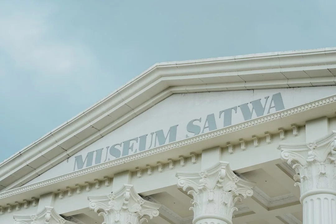 Auf der Fassade eines weißen Gebäudes mit klassizistischen Säulen steht unter einem wolkenverhangenen Himmel der Schriftzug "Museum Satwa", der auf die Bedeutung von Museumsbesuchen für die kulturelle Bildung hinweist.