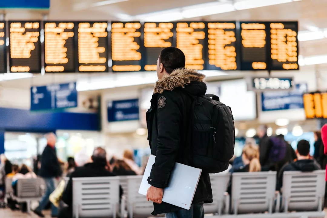 Eine Person mit Rucksack und Laptop steht in einem Flughafenterminal und schaut auf die Abflugtafel - eine häufige Szene in der Tourismusbranche, in der viele Reiseveranstalter den Reisenden bei der Navigation helfen.