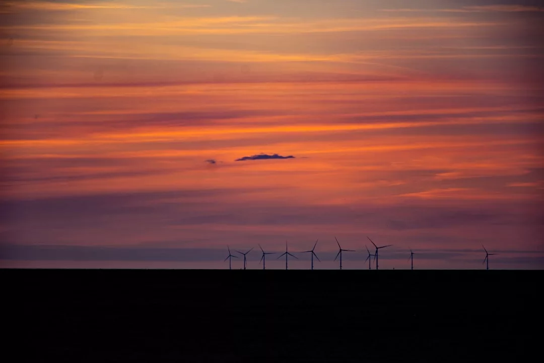 Windkraftwerke sind auf dem Horizont unter einem Sonnenuntergangshimmel mit orangefarbenen, pinken und violetten Tönen sichtbar und unterstreichen ihre Bedeutung für die moderne Energieversorgung.