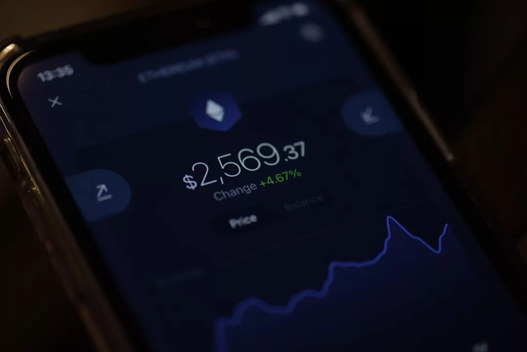 Ein Smartphone-Bildschirm zeigt einen Kryptowährungswert von 2.569,37 $ mit einem Anstieg von 4,67 % an, zusammen mit einem Liniendiagramm, das die jüngsten Preisänderungen anzeigt - ideal für diejenigen, die Finanz-Apps zur Verbesserung ihrer Geldverwaltung verwenden.