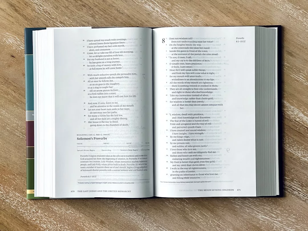 Ein aufgeschlagenes Buch liegt auf einer hölzernen Oberfläche und zeigt einen Textabschnitt mit dem Titel "Salomos Sprüche" mit schwarzem Text auf weißen Seiten. Am linken Rand sind farbige Registerkarten zu sehen - perfekt für kulinarische Inspiration oder zum Markieren deiner besten Kochbücher.