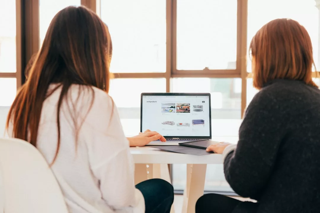 Zwei Personen sitzen an einem Tisch und schauen auf einen Laptop-Bildschirm, auf dem Online-Kurse für persönliche Entwicklung angezeigt werden.