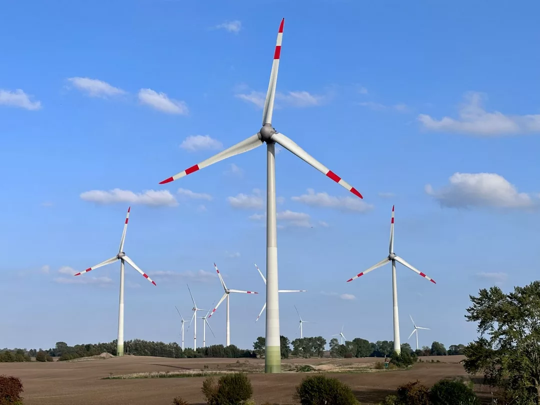 Eine Gruppe von Windturbinen steht auf einem flachen, offenen Feld unter einem klaren, blauen Himmel mit vereinzelten Wolken und veranschaulicht die Effizienz von Windturbinen und das Potenzial der modernen Windenergie.