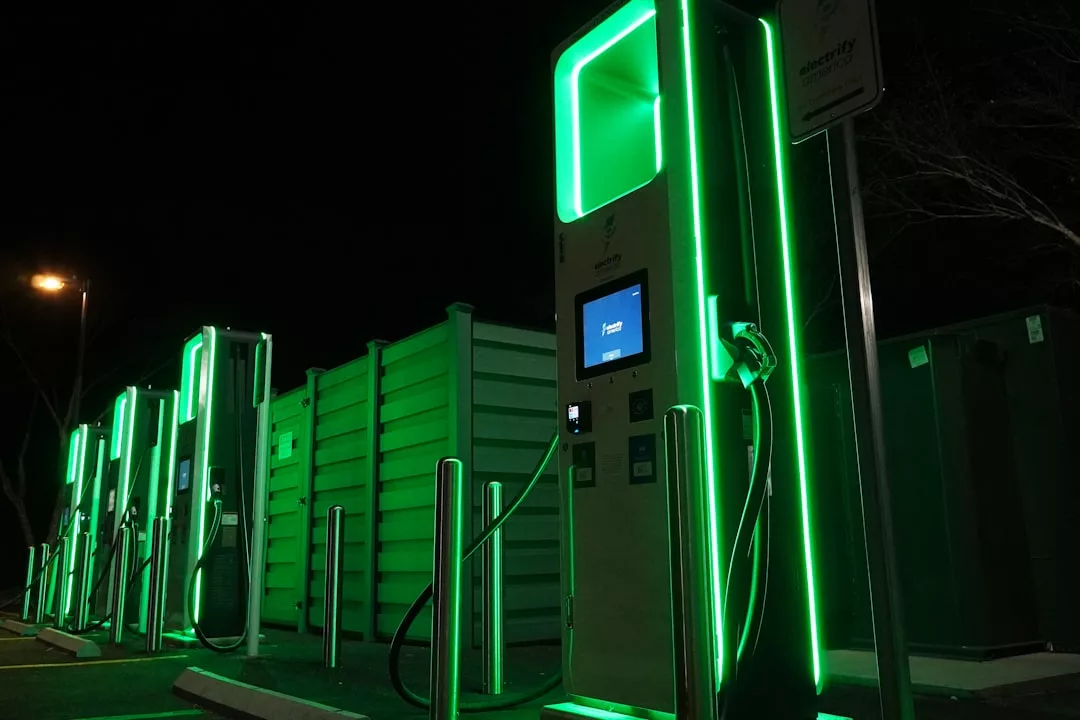 Mehrere Ladestationen für Elektrofahrzeuge sind nachts mit grünen Lichtern beleuchtet, ihre Bildschirme und Ladekabel sind sichtbar - ein Symbol für Nachhaltigkeit und die laufende Energierevolution.