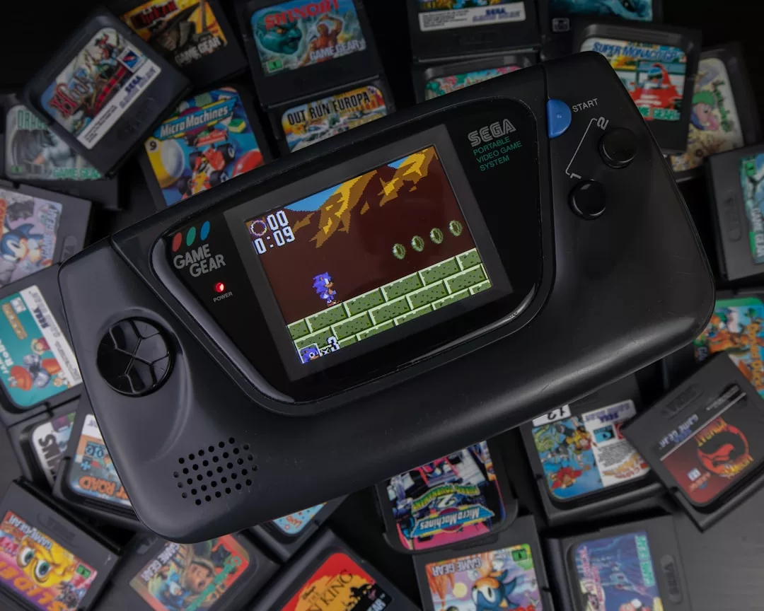 Eine Sega Game Gear Handheld-Konsole zeigt ein Jump'n'Run-Spiel, umgeben von verschiedenen Spielkassetten darunter - perfekt für eine kulturelle Analyse klassischer Videospiele.