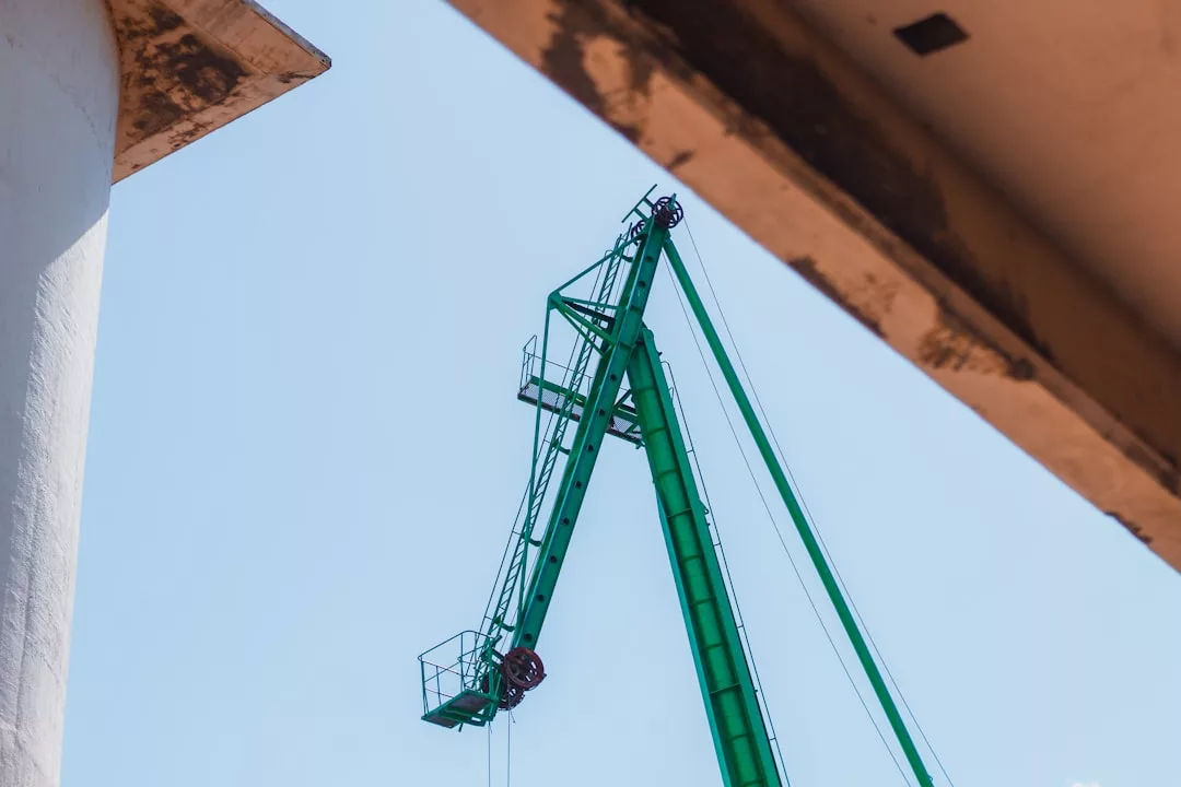 Ein grüner Industriekran ragt in den blauen Himmel, umrahmt von den Kanten zweier großer Betonstrukturen - die perfekte Szene für Urban Exploring-Enthusiasten, die sich von der Faszination versteckter Stadträume angezogen fühlen.