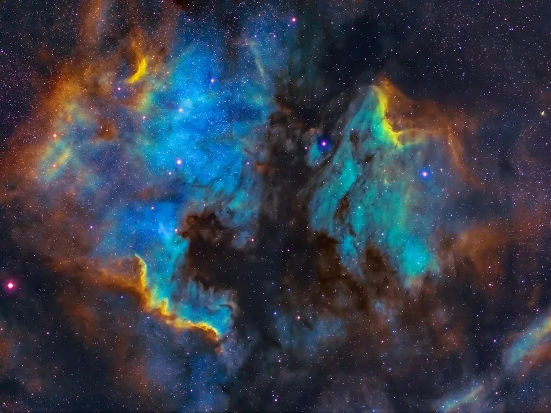 Farbenfrohes Bild eines Nebels in den Tiefen des Weltraums mit leuchtend blauen, gelben und orangefarbenen Gas- und Staubwolken und verstreuten Sternen - ein atemberaubender Einblick in die faszinierende Welt der Astronomie.