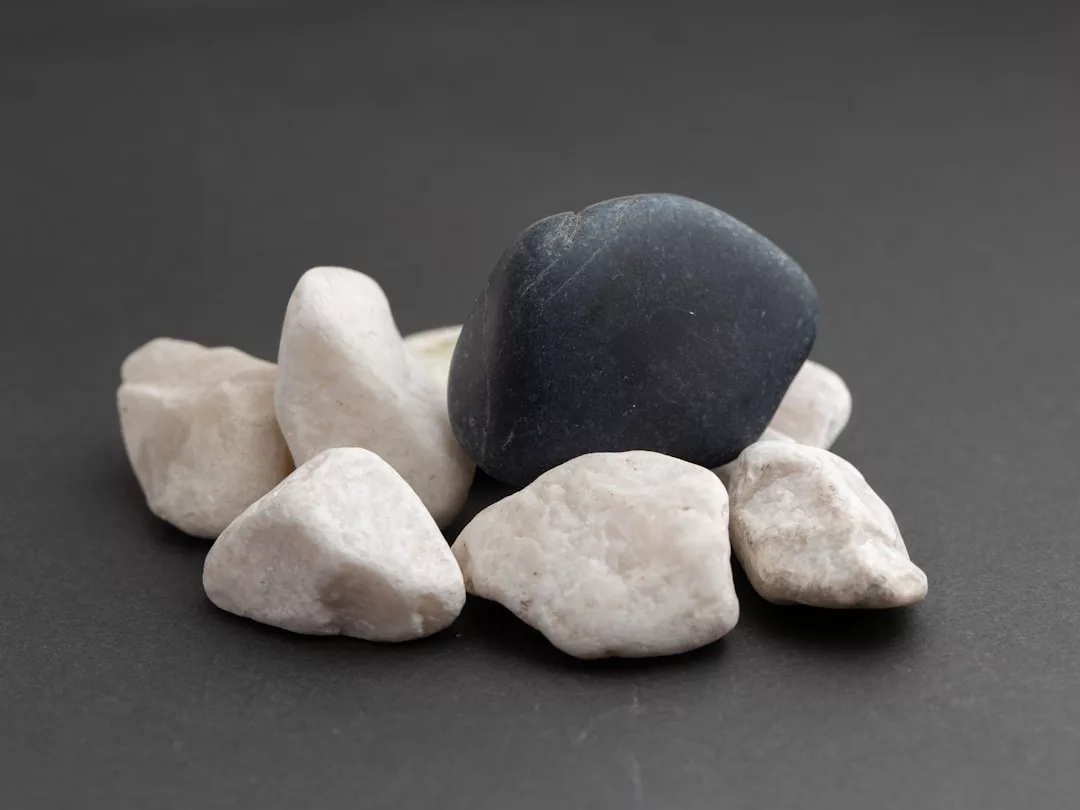 Sechs weiße Heilsteine und ein größerer dunkler Stein sind auf einem schlichten dunklen Hintergrund angeordnet und laden dazu ein, die Heilsteine Wirkung sowie ihre heilende Kraft zu entdecken.