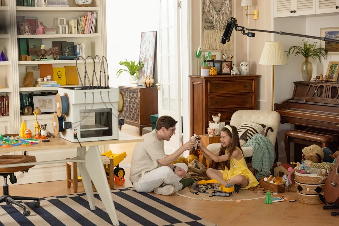 Ein Erwachsener und ein Kind sitzen auf dem Boden und bauen in einem überfüllten Wohnzimmer Spielzeug zusammen, umgeben von Büchern, Plüschtieren und einem sichtbaren Mikrofon für die Filmproduktion, das die Integration von Kindern und Technologie in den Alltag festhält.
