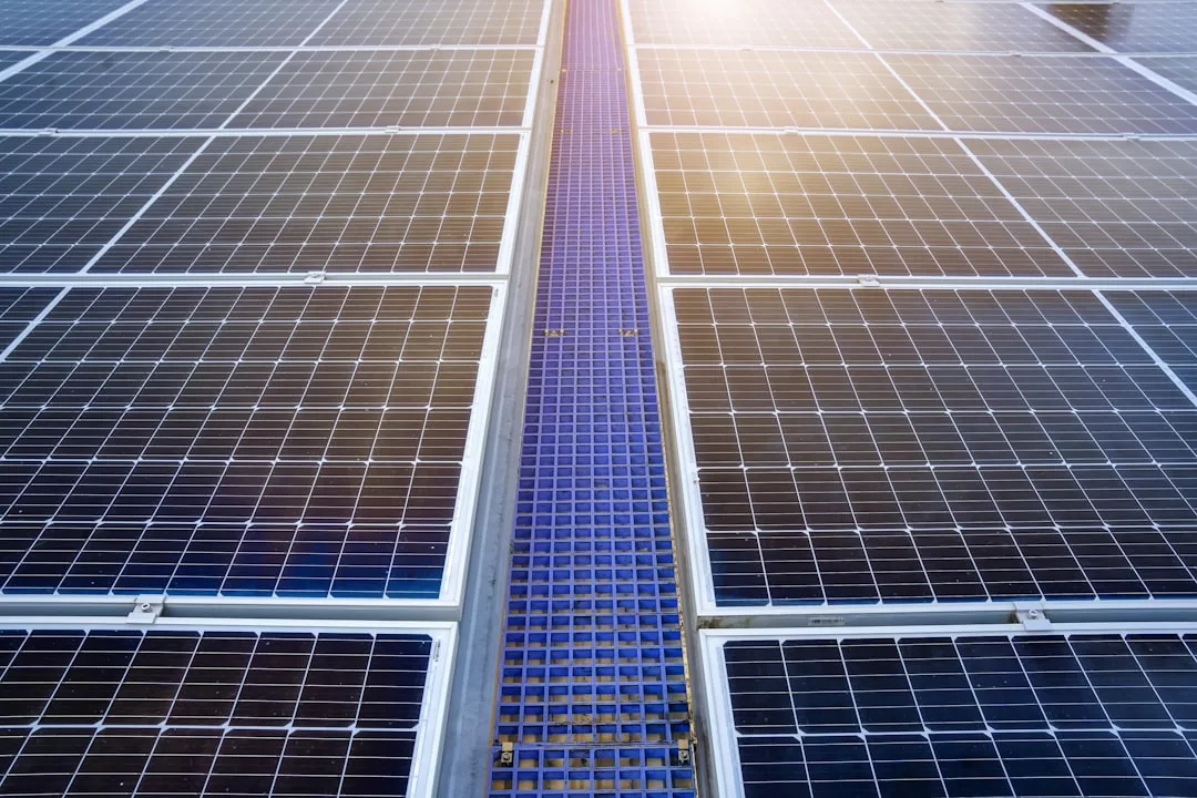 Nahaufnahme von reihenweise angeordneten Solarmodulen, die das Sonnenlicht reflektieren und in deren Mitte eine blaue Gitterstruktur verläuft, die die Solarenergie als wirtschaftliche Investition in die Zukunft hervorhebt.