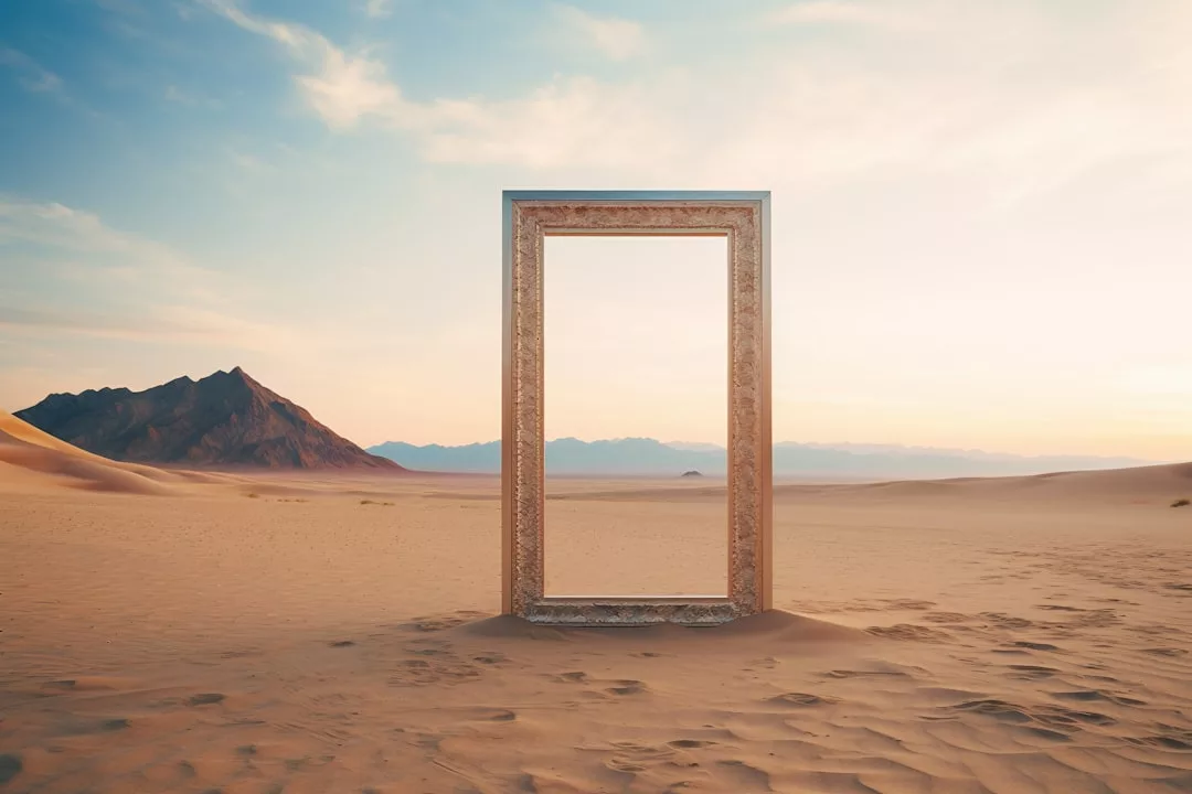 Ein großer, verschnörkelter, leerer Bilderrahmen steht aufrecht inmitten einer Wüste und symbolisiert die spirituelle Transformation inmitten von Sanddünen und fernen Bergen unter einem teilweise bewölkten Himmel.