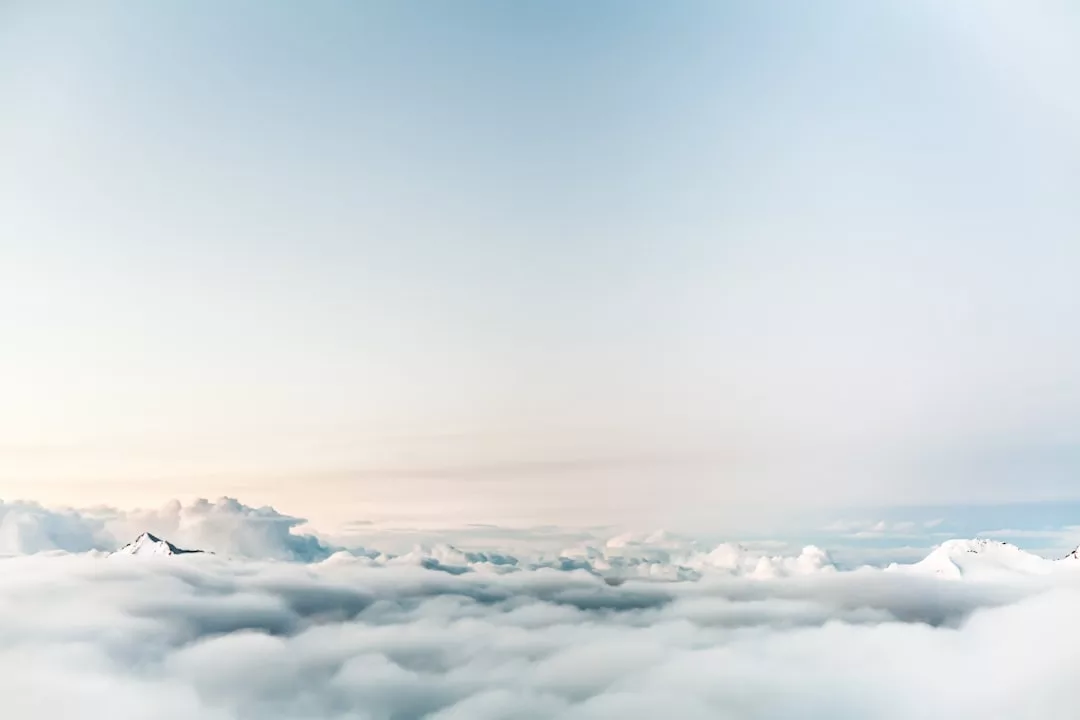 Wolken bedecken die Berggipfel unter einem hellen, klaren Himmel mit sanftem Licht am Horizont, das an Zen-artige Gelassenheit und die Kunst des Lebens erinnert.