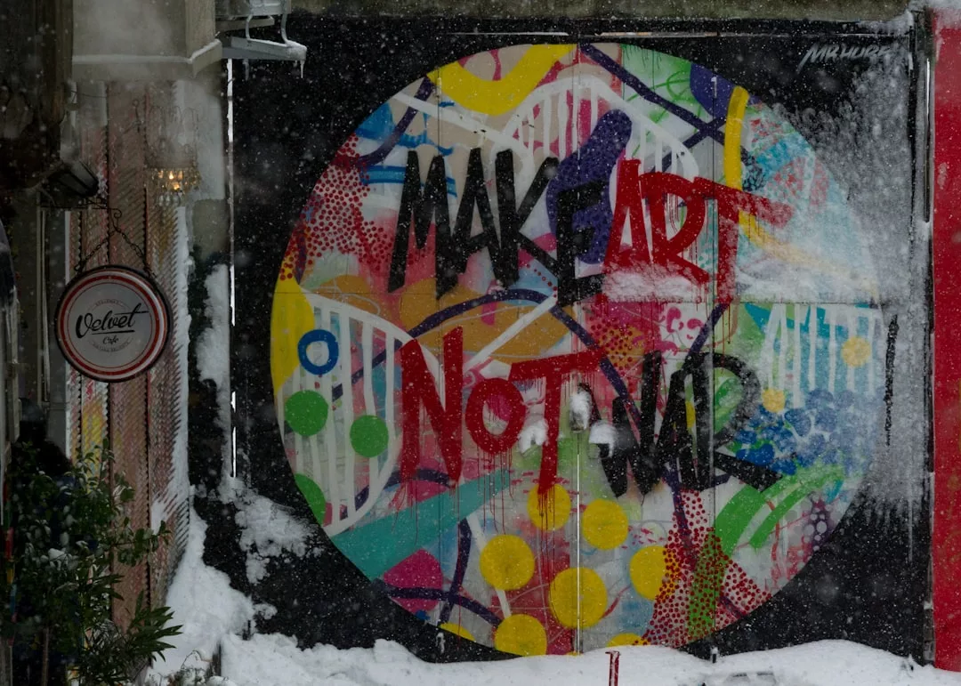 Ein farbenfrohes, urbanes Kunst-Graffiti mit dem Text "MAKE ART NOT WAR" ist auf eine Wand gemalt, umgeben von Schnee auf dem Boden.