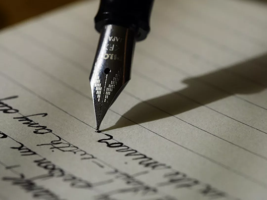 Eine Nahaufnahme eines Füllfederhalters, der auf liniertem Papier schreibt, wobei die handschriftliche Kalligraphie und die kursive Schrift teilweise sichtbar sind und ein Gefühl von formaler Eleganz vermitteln.