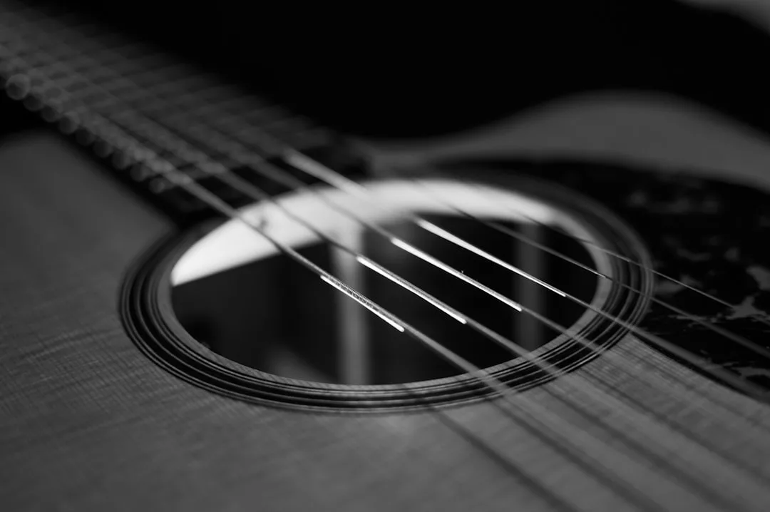 Nahaufnahme einer Akustikgitarre in Schwarz-Weiß, die sich auf die Saiten und das Schallloch konzentriert und die Kunst des Musikmachens im Detail festhält.