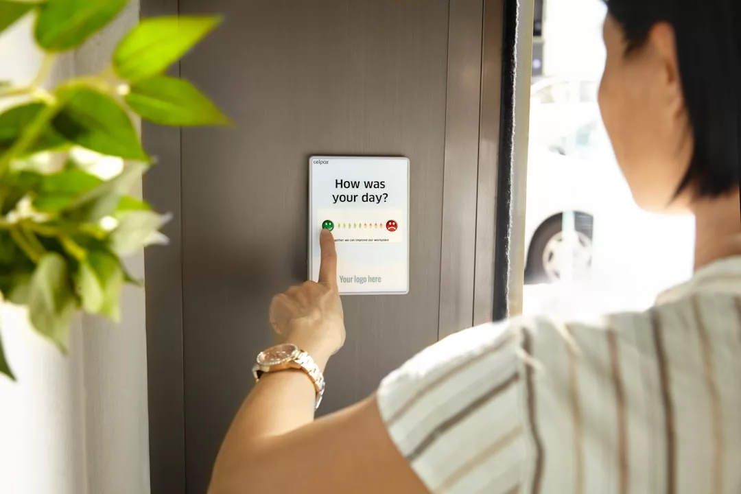 Eine Person drückt ein Smiley auf einem an der Wand montierten Touchscreen, der die Frage "Wie war Ihr Tag?" stellt, und macht professionelles Feedback einfach und direkt zugänglich.