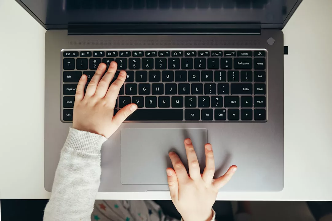 Die Hände eines Kleinkindes, das auf einer schwarzen Laptop-Tastatur tippt, von oben betrachtet - ein Einblick in die Art und Weise, wie Technologie die moderne Bildung von klein auf prägt.