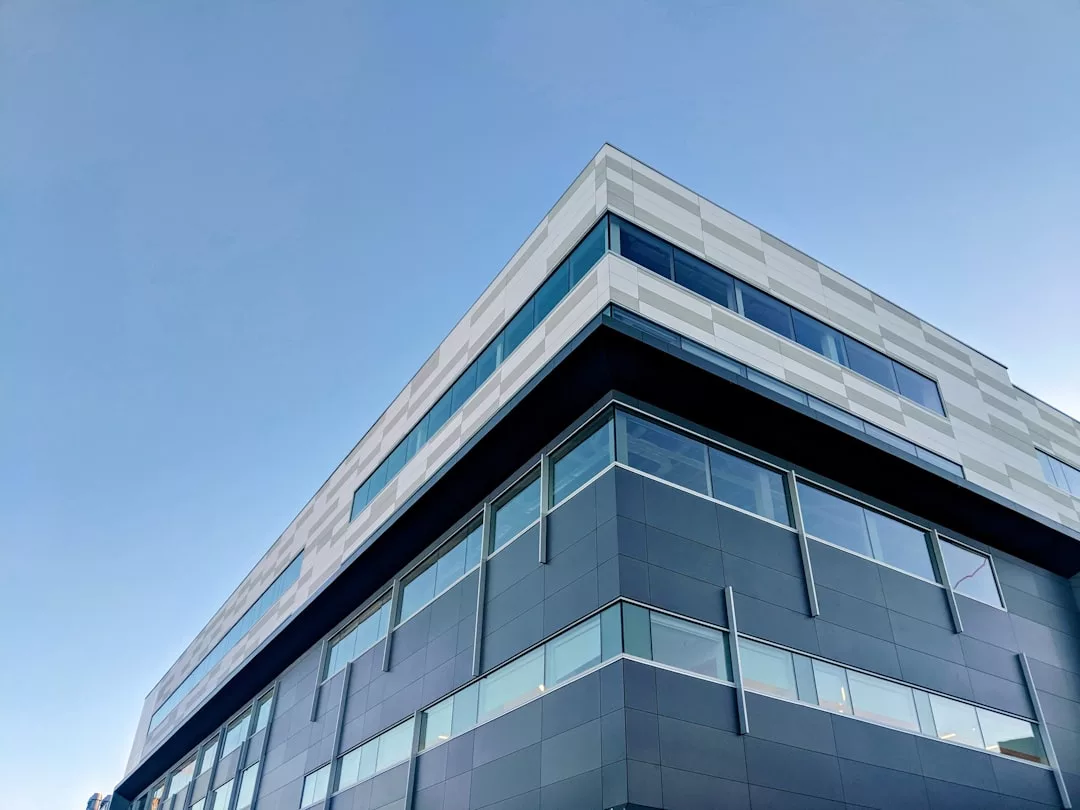 Ein modernes mehrstöckiges Gebäude mit spiegelnden Fenstern, verkleidet mit schwarzen und weißen Platten, von einem niedrigen Winkel aus gesehen vor einem klaren blauen Himmel - eine ideale Kulisse für innovative Unternehmensentwicklung oder Private-Equity-Unternehmungen.