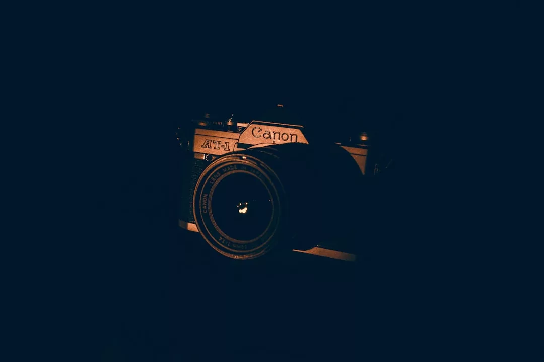 Eine Canon AT-1 Filmkamera ist im Dunkeln teilweise erleuchtet, wobei ihre Schönheit und der Markenname besonders hervorgehoben werden - ein Moment moderner Fotokunst.