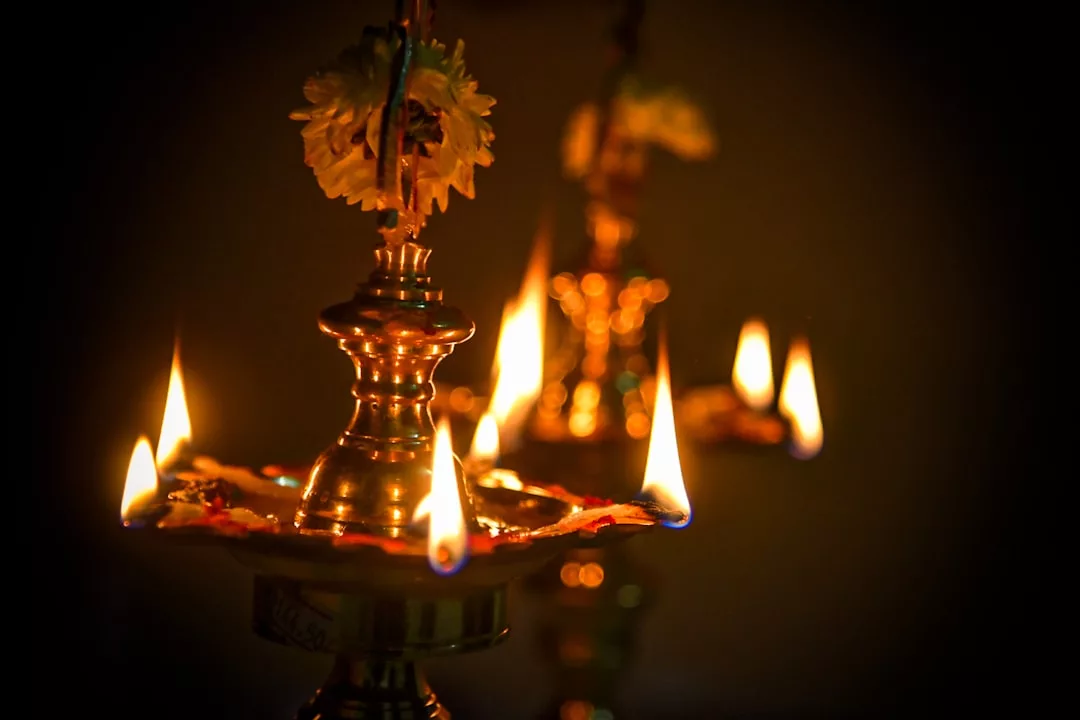 Eine Öllampe aus Messing mit mehreren Flammendochten wird angezündet, ist mit Blumen verziert und steht vor einem dunklen Hintergrund, der Spiritualität und die Suche nach Erleuchtung symbolisiert.
