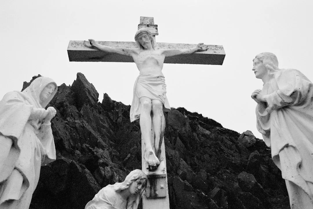 Ein steinernes Kruzifix mit einer Darstellung von Jesus am Kreuz, flankiert von drei Trauernden, vor einem felsigen Hintergrund, erinnert an die Tiefe der Mystik, die das Herzstück der christlichen Mystik ist.