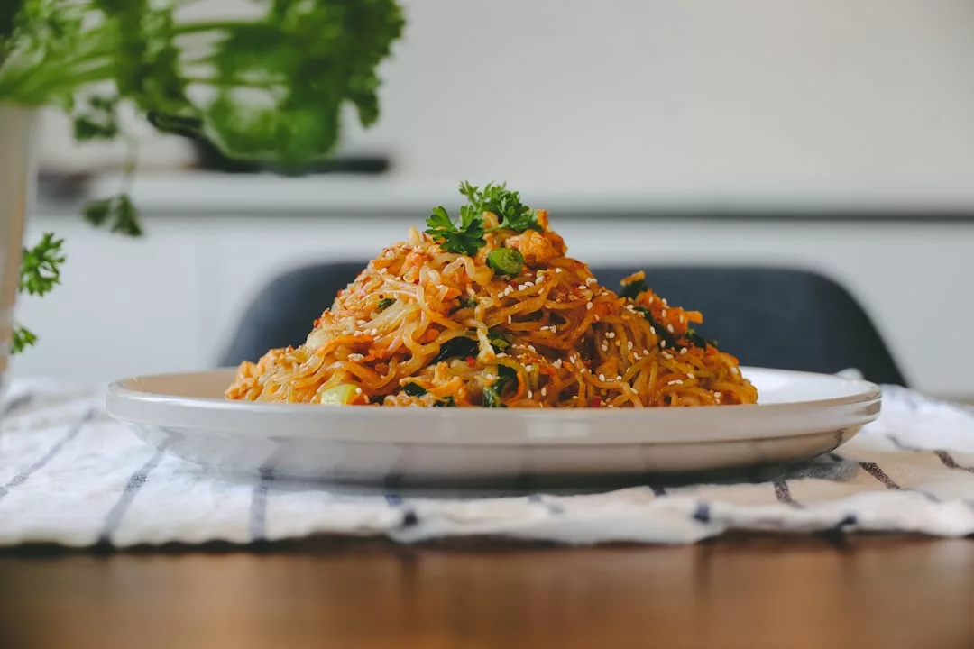 Ein Teller mit gebratenen Nudeln mit Gemüse und Beilagen liegt auf einem weißen Tuch, fotografiert in einem Innenraum mit sanfter Beleuchtung - ideal für alle, die die Vorteile einer Low-Carb-Diät suchen.