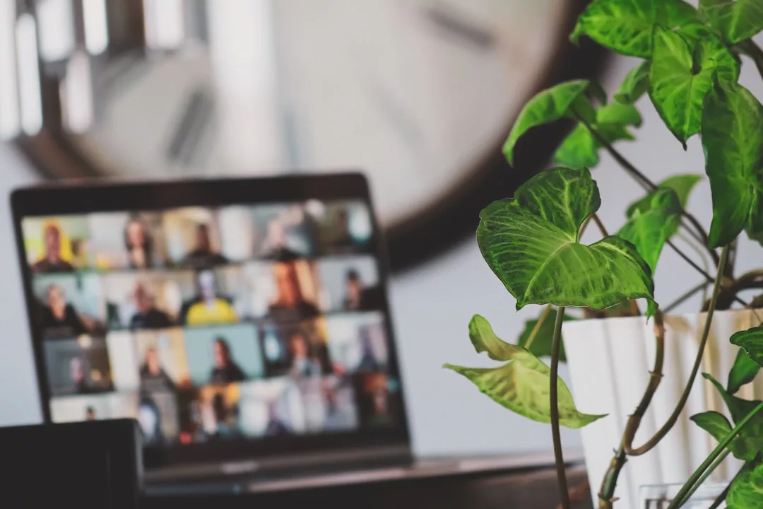 Ein Laptop zeigt eine Videokonferenz mit mehreren Teilnehmern in einem Raster-Layout an; im Vordergrund steht eine grüne Topfpflanze im Mittelpunkt, die die Vorteile vom Remote-Arbeiten im gemütlichen Homeoffice hervorhebt.