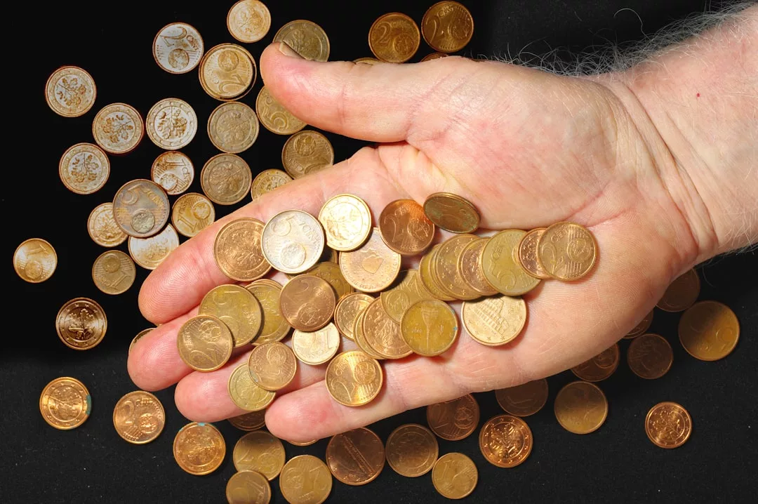Eine Hand hält einen Haufen verschiedener Kupfermünzen und lässt sie wieder los - als Symbol für die Vorteile, die Crowdfunding für Start-ups mit sich bringt - während weitere Münzen auf einer schwarzen Fläche darunter verstreut sind.