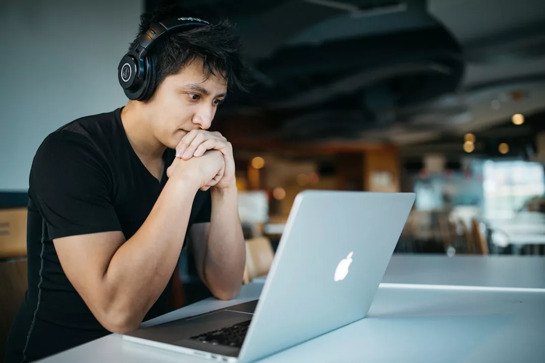 Eine Person mit Kopfhörern sitzt an einem Tisch und schaut konzentriert auf einen Laptop in einem modernen, gut beleuchteten Innenraum - und genießt flexibles Lernen und Online-Kurse bequem von Zuhause.
