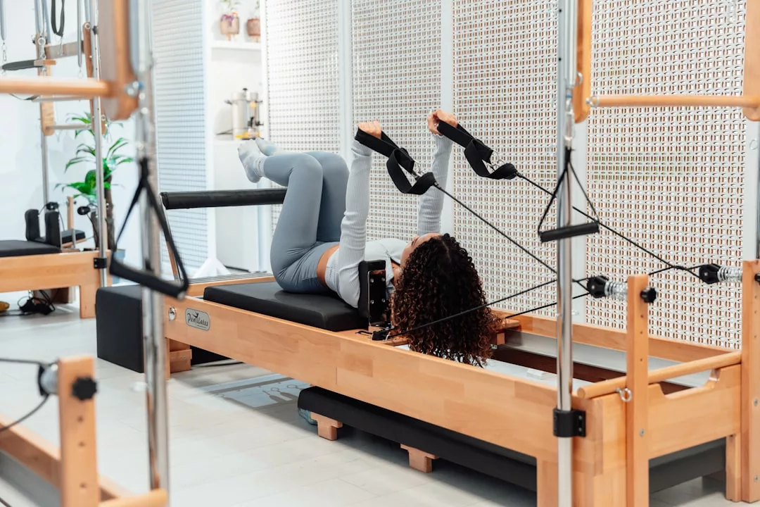 Person liegt auf einem Pilates Reformer und trägt Sportkleidung, mit den Füßen in den Schlaufen und Armen entspannt an der Seite - perfektes Training für starke Körperhaltung und alle Vorteile von Pilates im modernen Fitnessstudio.